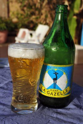 Bière locale Gazelle dans un verre et sa bouteille, servie fraîche au Campement Buhanor, idéale pour se rafraîchir à la plage Cap-Skirring. 