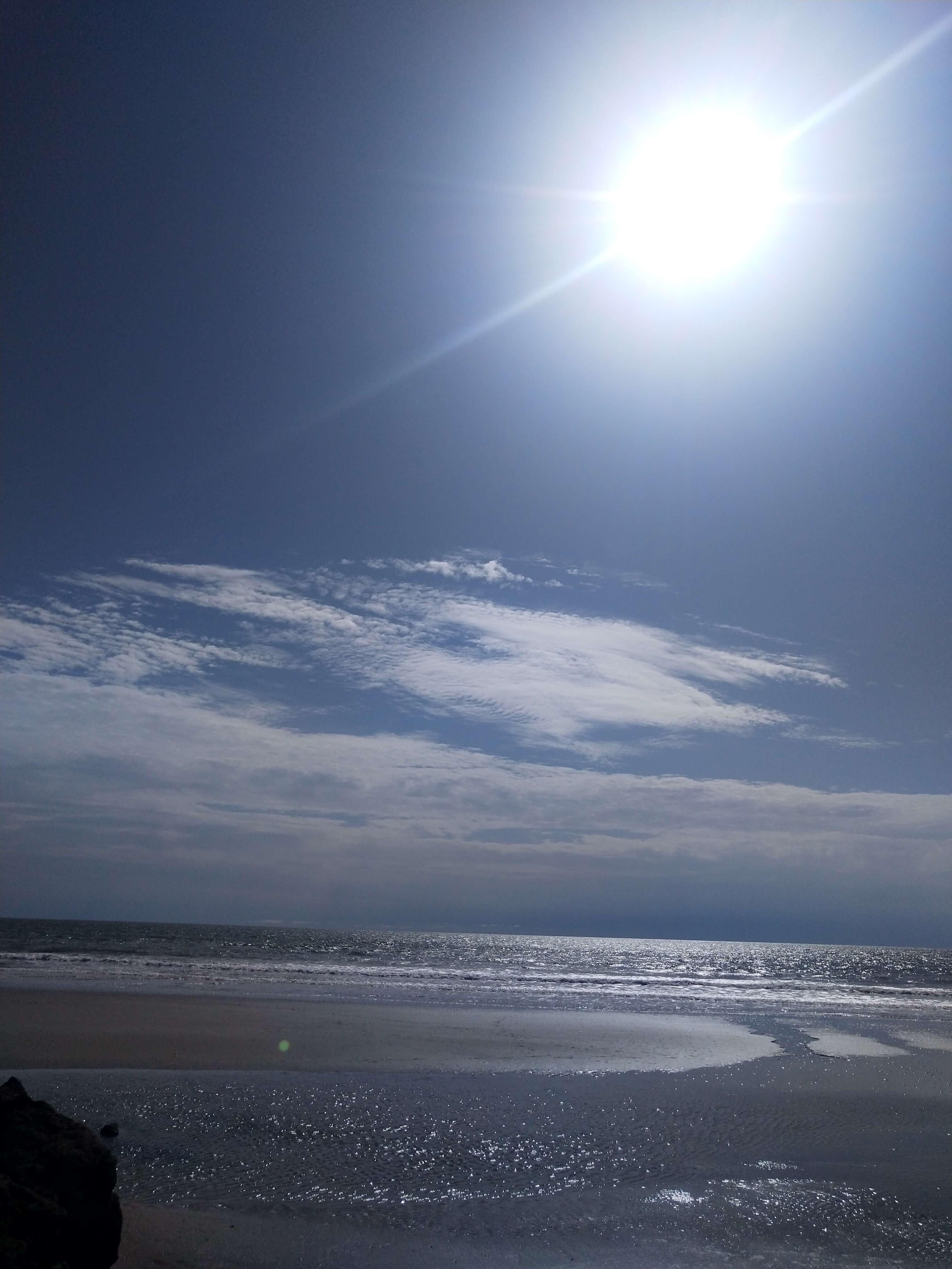 Plage de Cap-Skirring en pleine journée, avec un ciel bleu lumineux et le soleil éclatant sur l'océan Atlantique, invitant à la baignade et à la détente près du Campement Buhanor.