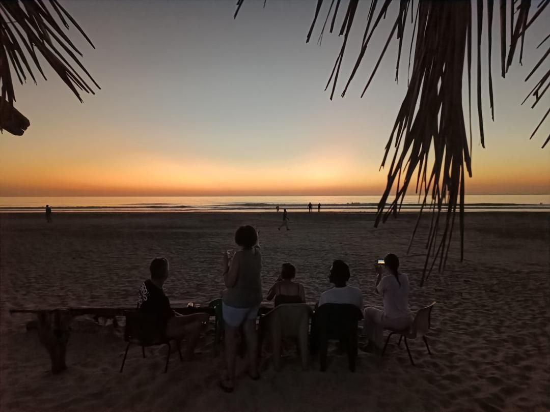 Groupe d'amis ou de familles admirant le spectaculaire coucher de soleil sur la plage de Cap-Skirring, savourant un moment convivial au Campement Buhanor.