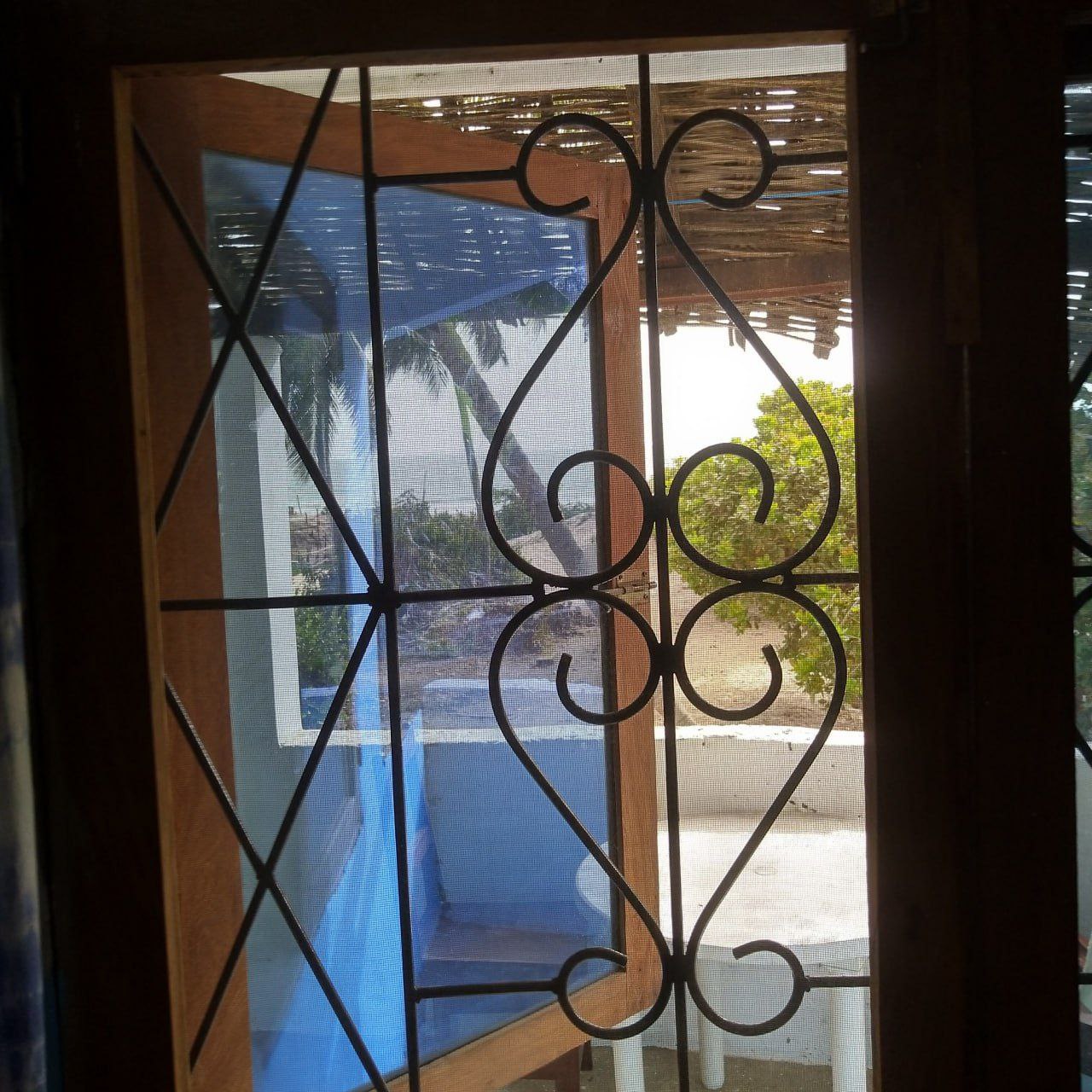 Détail d'une grille de fenêtre en fer forgé aux motifs artistiques, reflétant l'artisanat et l'esthétique locale du Campement Buhanor à Cap-Skirring.