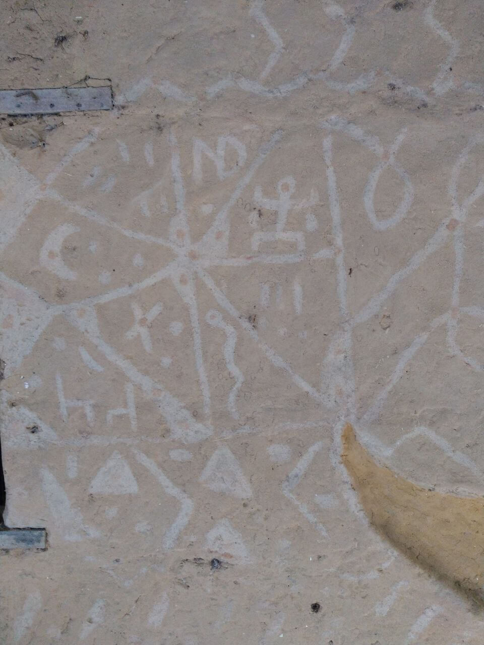 Mur d'un bâtiment traditionnel Diola au Campement Buhanor, orné de motifs linéaires et géométriques peints en bleu clair, illustrant l'artisanat et l'architecture culturelle de la Casamance.