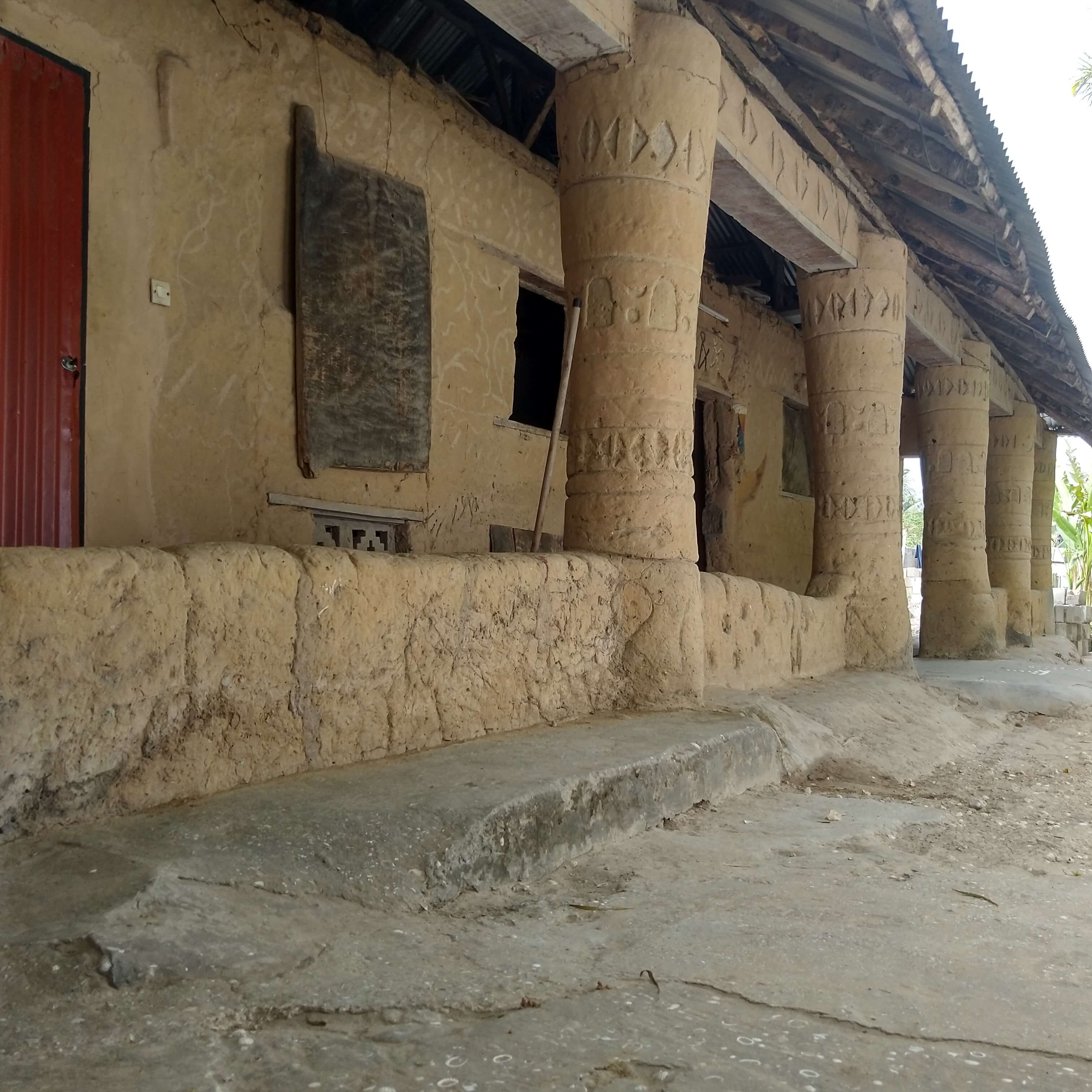 Façade d'un bâtiment traditionnel Diola au Campement Buhanor, caractérisée par des piliers massifs et sculptés, des murs en terre et un toit de chaume, reflétant l'architecture authentique de la Casamance.