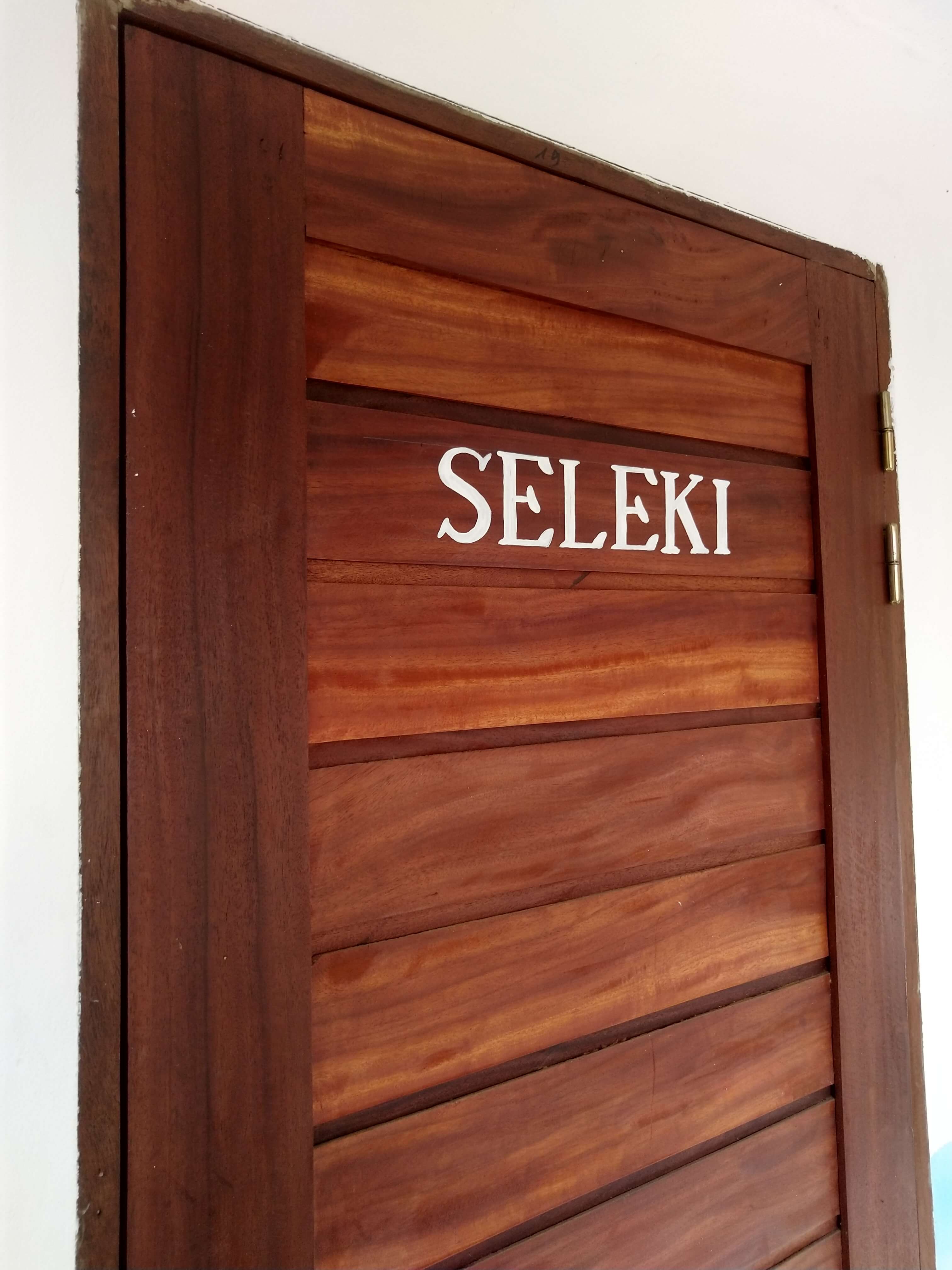  Porte en bois de la chambre Seleki au Campement Buhanor, invitant à découvrir l'un de nos hébergements confortables à Cap-Skirring. 