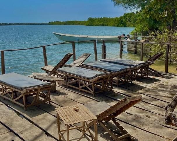Transats en bois sur une jetée flottante sur l'île d'Egueye, offrant une vue sur l'eau turquoise et les mangroves, idéal pour une journée de détente au départ du Campement Buhanor.