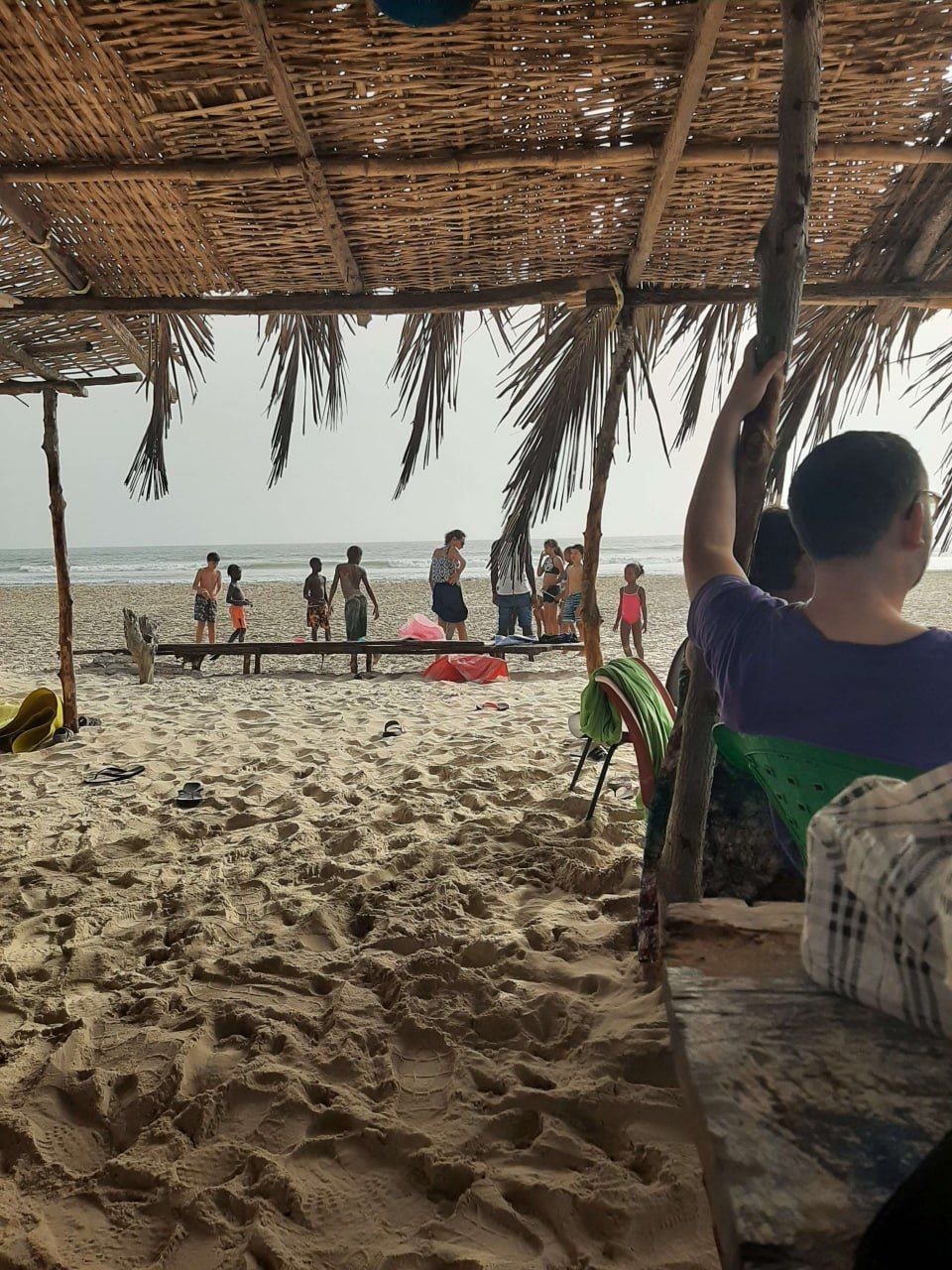 Groupe de personnes profitant de la plage de Cap-Skirring sous une paillote ombragée du Campement Buhanor, idéal pour les jeux et la détente en bord de mer.